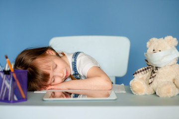 A girl 5-6 years old sitting at a table performs homework remote tasks on the tablet. Isolate on a...