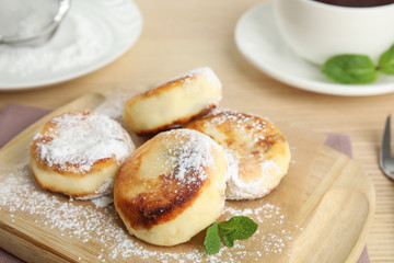 Delicious cottage cheese pancakes with sugar powder on wooden board, closeup