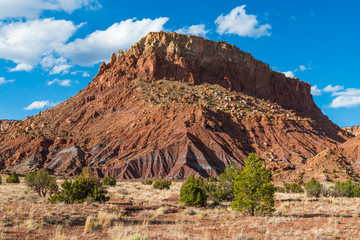 A colorful mesa under a beautiful blue sky above a desert floor of grasses and juniper trees