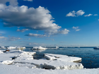 The coast of the Finnish Gulf . Spring. Snow-covered shore and bay, freed from ice. Blue sky and clouds.There are many floating ice floes in the water. Cold. There are traces on the snow.