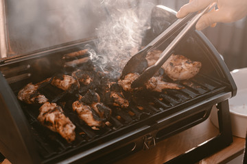 Grill season outdoor in park or balcony. Spring summer grilling. Balcony gas grill. Barbeque fourth of July weekend. Chicken wings on grill. Flame and smoke over grill. BBQ quarantine on balcony.