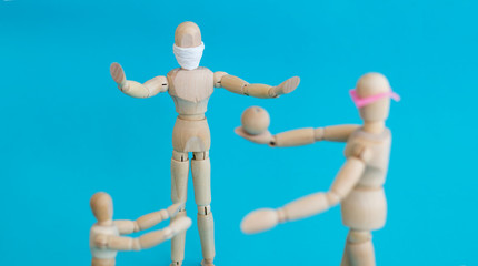 Concept - ban on ball games with children during quarantine. Group of wooden little men mannequins. A man in a protective medical mask prohibits others from playing actively. Social distance.