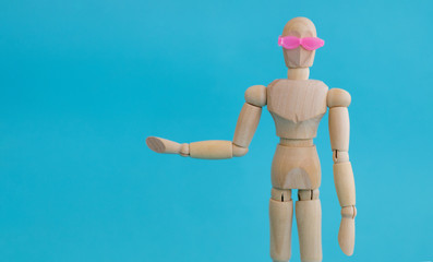 Wooden man puppet in pink glasses pointing in left on blue background.