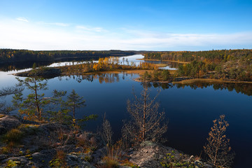 Peak. It has several pines, a dry tree, stones and moss. In the middle of the channel are an islet and trees decorated with yellow and red foliage. Still water with reflected trees and sky.