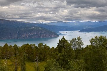 Hanging, with leaden clouds, the sky. The twisting course of the fjord. Azure water. Beautiful, granite coast. Ahead there are many trees and a clearing with grass. Severe, beautiful Norwegian nature.