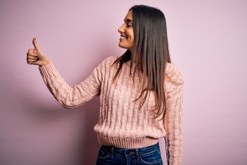 Young beautiful brunette woman wearing casual sweater over isolated pink background Looking proud, smiling doing thumbs up gesture to the side