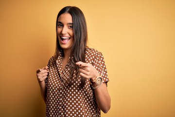Young beautiful brunette woman wearing casual shirt over isolated yellow background pointing fingers to camera with happy and funny face. Good energy and vibes.