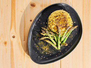 Vegan Risotto with Asparagus and Curry (no butter), on a dark plate on a wooden table.