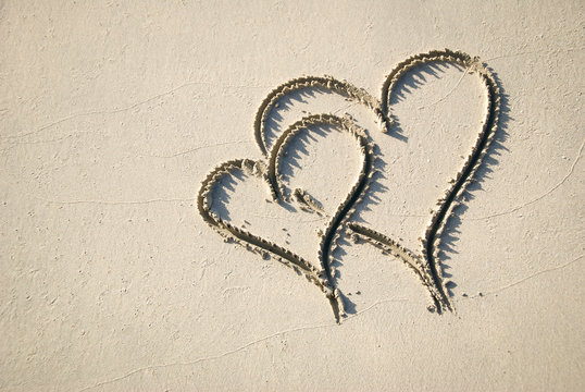 Pair of handwritten hearts drawn interlocking in smooth sand on a sunny beach