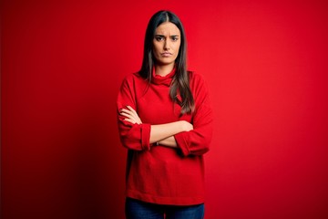 Young beautiful brunette woman wearing casual sweater over isolated red background skeptic and...