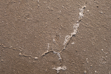 Sandy bottom of a dried reservoir with cracks and salt crystals.