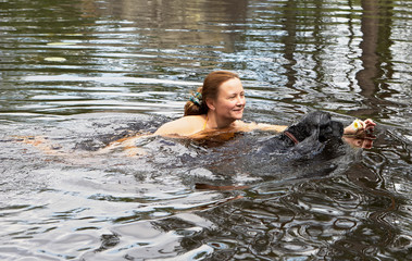 A middle-aged woman is swimming along the water with an English cocker spaniel. In her left hand she holds a lily flower and smiles. Summer. Russia.