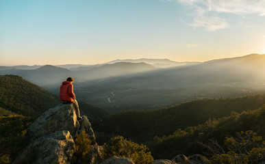Young boy sitting on rocks watching a mountain landscape, with an incredible sunset, warm sky with...