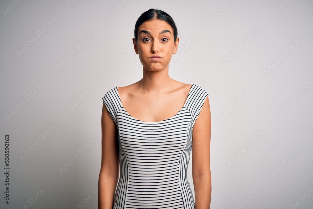 Wall mural young beautiful brunette woman wearing casual striped dress over isolated white background puffing c