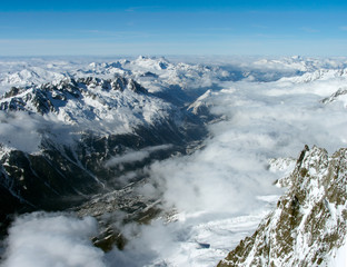 French Alps. Winter. From the top of the mountain peak there is a beautiful view of the valley and mountain ranges. In the foreground is a part of the rock and clouds.