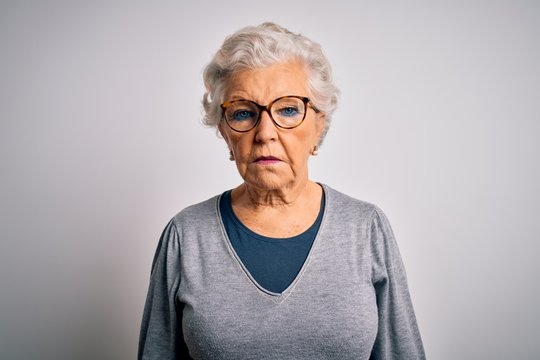 Senior beautiful grey-haired woman wearing casual sweater and glasses over white background with serious expression on face. Simple and natural looking at the camera.