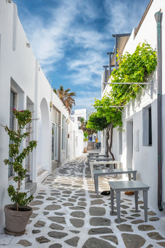 Picturesque narrow street with traditional whitewashed houses with cafe tables of Naousa town in famous tourist attraction Paros island, Greece