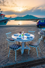 Street cafe table with ready for dinner on quay of Naousa town port in famous tourist attraction Paros island, Greece on sunset