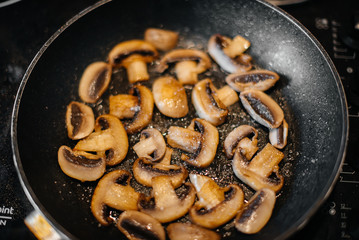 Thinly sliced fresh raw mushrooms are fried in a pan close-up. Healthy diet