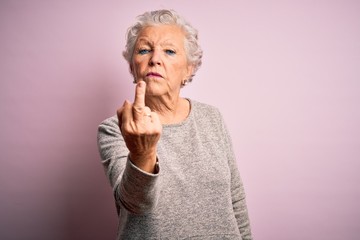 Senior beautiful woman wearing casual t-shirt standing over isolated pink background Showing middle finger, impolite and rude fuck off expression