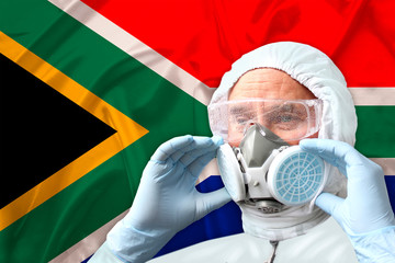 Fototapeta na wymiar male doctor, disinfector in a protective suit, respirator, goggles on the background of the silk national flag of South Africa, the concept of biological, chemical weapons, coronavirus, COVID-19