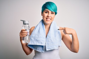 Young sporty woman with blue fashion hair holding bottle of water wearing towel after do sport with surprise face pointing finger to himself