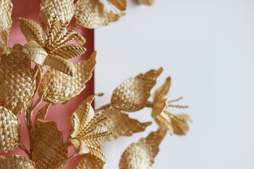 Fototapeta na wymiar Branch with leaves and flowers is made of straw. Straw wall decoration. The products are made of straw. Decoration of straw on a pink white background