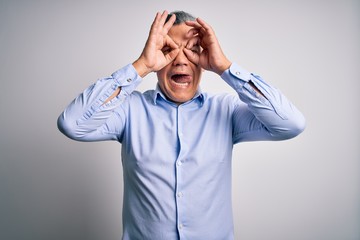 Middle age handsome grey-haired business man wearing elegant shirt over white background doing ok gesture like binoculars sticking tongue out, eyes looking through fingers. Crazy expression.