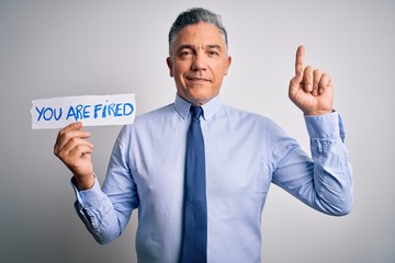 Middle age grey-haired man fired with problems holding paper with you are fired message surprised with an idea or question pointing finger with happy face, number one