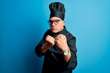 Middle age handsome grey-haired chef man wearing cooker uniform and hat Ready to fight with fist defense gesture, angry and upset face, afraid of problem