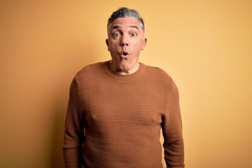 Fototapeta premium Middle age handsome grey-haired man wearing casual sweater over yellow background afraid and shocked with surprise expression, fear and excited face.