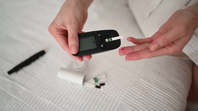 Diabetes checking blood sugar level. Woman using lancelet and digital glucometer at home. Medicine, diet diabetes, health care concept - female hands with glucometer checking body glucose level