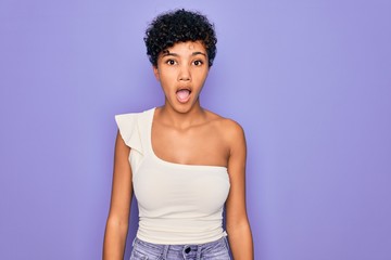 Young beautiful african american afro woman wearing casual t-shirt over purple background afraid and shocked with surprise and amazed expression, fear and excited face.