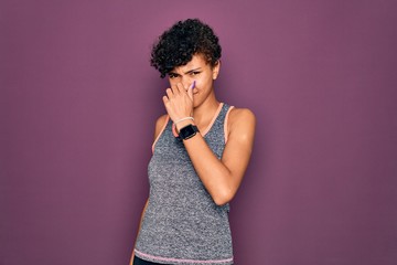 Fototapeta na wymiar Young beautiful african american afro sportswoman doing exercise wearing sportswear smelling something stinky and disgusting, intolerable smell, holding breath with fingers on nose. Bad smell