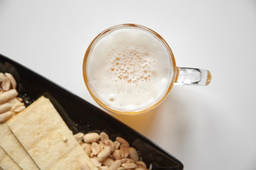 Mug of unfiltered light wheat beer with beer snacks on white table