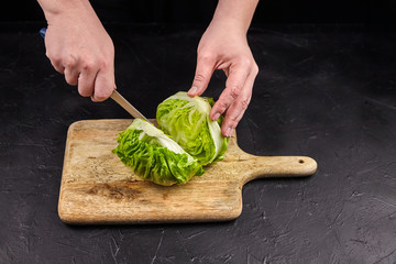 Person cuts iceberg lettuce on wooden chopping board