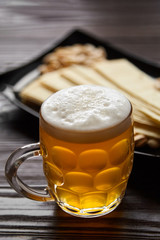 Mug of unfiltered light wheat beer with beer snacks on wooden table