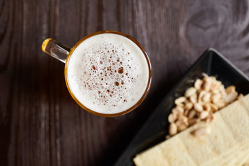 Mug of unfiltered light wheat beer with beer snacks on brown wooden table, top view