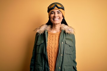 Young beautiful hispanic woman wearing ski glasses and coat for winter weather with a happy and cool smile on face. Lucky person.