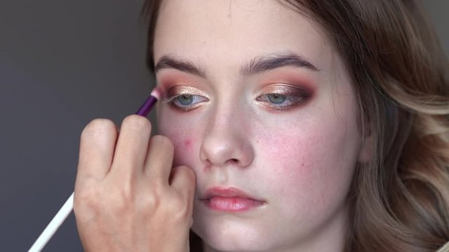 Girl makeup artist paints the eyelids of a girl model