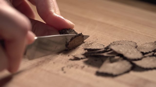 A young lady is slicing up a piece of black truffle for a dish at home for dinner.