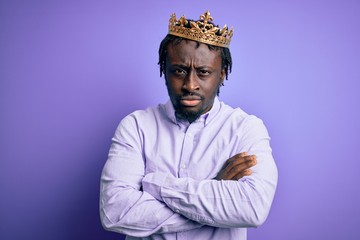 Young african american man wearing golden crown of king over isolated purple background skeptic and nervous, disapproving expression on face with crossed arms. Negative person.