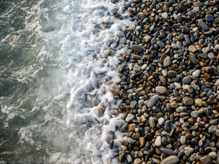 Pebbles at the coastline are washed by the sea waves water. Top view from above. Perfect for wallpaper, background for tourism, art or meditation design projects.