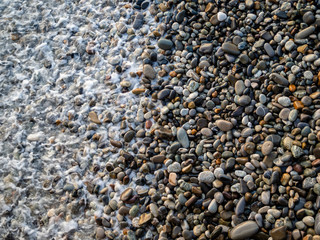 Pebbles at the coastline are washed by the sea waves water. Top view from above. Perfect for wallpaper, background for tourism, art or meditation design projects.