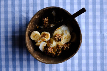 yoghurt with banana slices, coconut and granola, healthy snack in coconut bowl