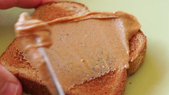 Spreading creamy peanut butter on whole wheat toast, healthy breakfast choice, 4k