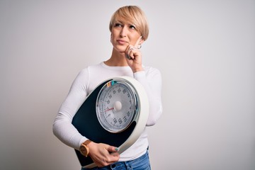 Young blonde woman with short hair holding scale for healthy weight and lifestyle serious face...