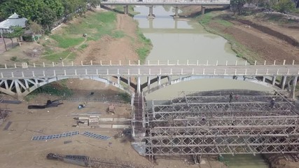 aerial sliding shot of workers working on a scaffolding structure of the new bridge near the old one.  It is would be expected to ease the congestion of traffic in town