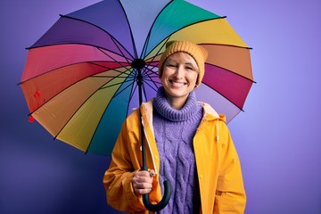 Young blonde woman with short hair wearing waterproff raincoat and colorful umbrella with a happy...