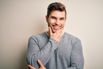 Young handsome blond man with beard and blue eyes wearing casual sweater looking confident at the camera smiling with crossed arms and hand raised on chin. Thinking positive.